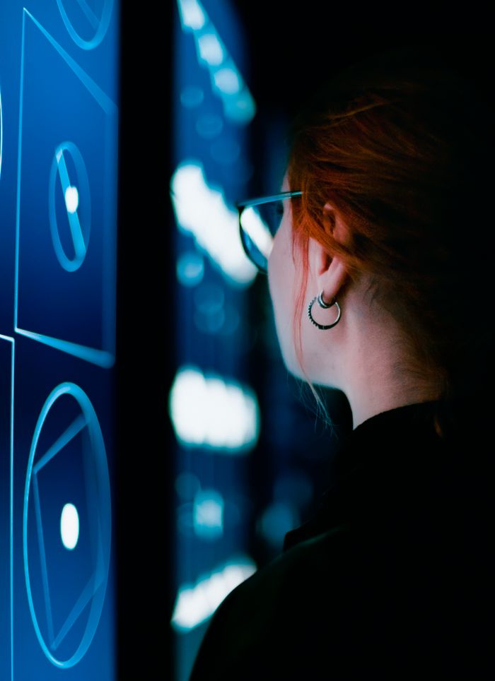A woman with eyeglasses interacts with an illuminated digital screen, showcasing modern technology.
